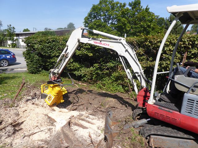 Stubbenfräse ART-1-001 – live bei der Baumstumpf-Fräsarbeit, montiert an Takeuchi-Minibagger, Fahrer sichtbar, Garten-/Straßenkulisse