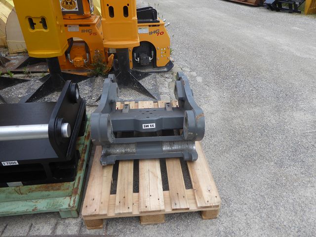 SW-Adapterplatte SW 66 ART-271-105 – Übersichtsaufnahme im Lagerhof, Etikett 'SW 66', daneben Fremdartikel mit Etikett 'L7000' sowie Hydraulikhämmer 'IHC 75'/'IHC 70' im Hintergrund